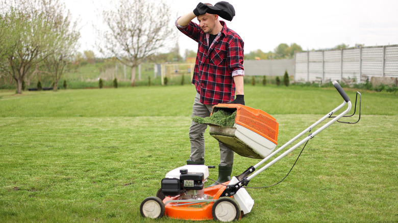 A person wiping sweat from their forehead while mowing grass