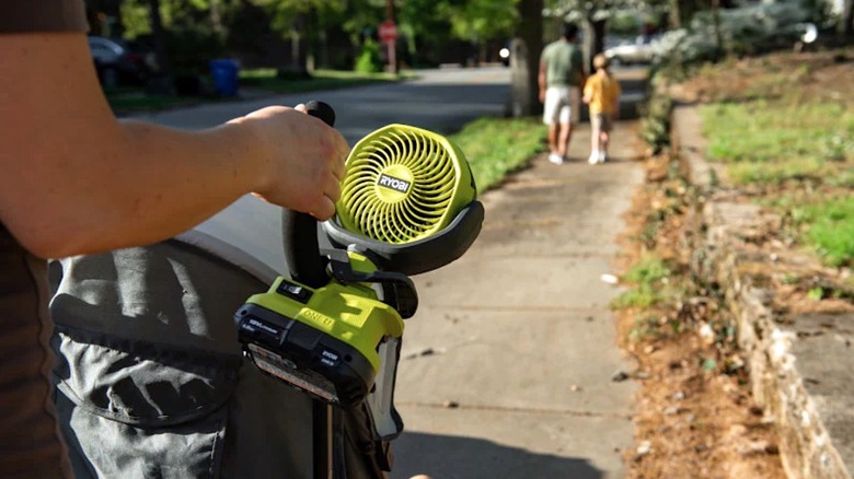 A person using a Ryobi clamp fan on a daily walk while pushing a stroller