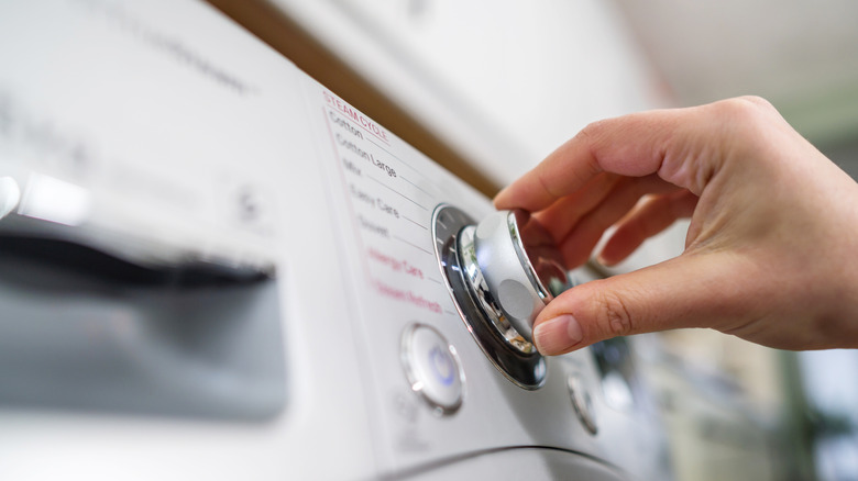 A person turns the dial of a washing machine.