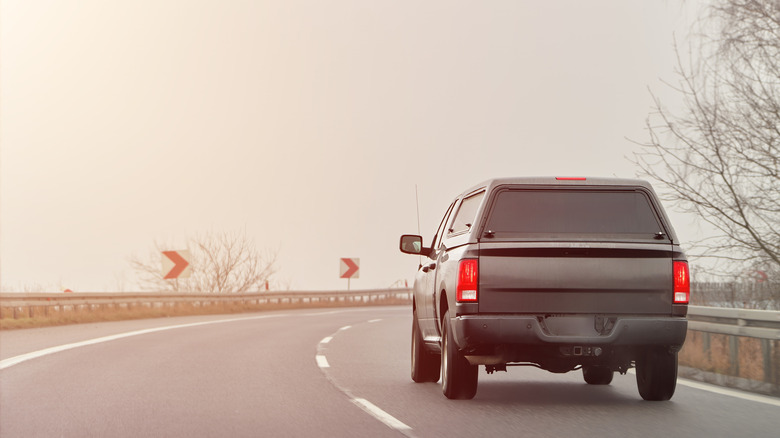Third-gen Ram pickup truck fitted with bed cap driving along road, rear-view