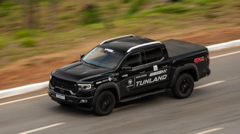 Ram crew-cab commercial truck driving along highway fitted with soft tonneau cover, front-left 3/4 view