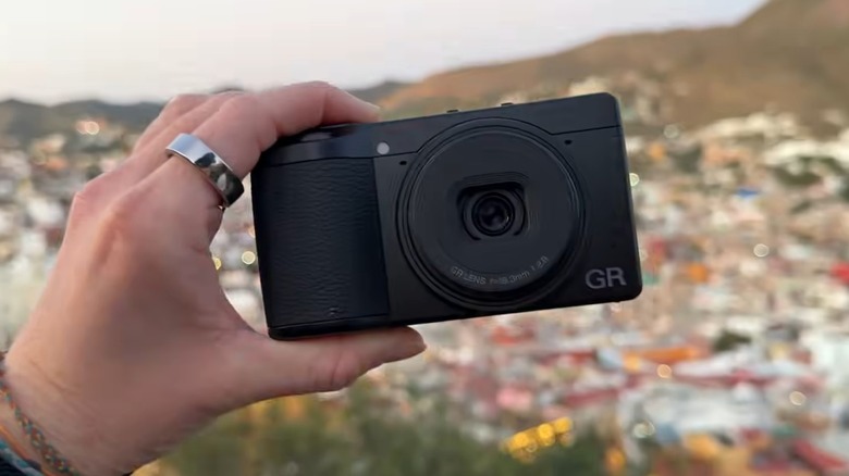 A person holding a Ricoh GR IV camera outside.