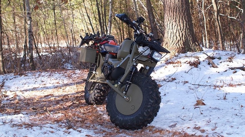 An olive green Rokon Trail-Breaker sitting on a snowy trail in the middle of a forest.