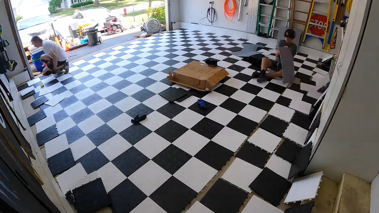 Two people installing the MotoFloor garage floor tiles inside of a garage, wide angle CCTV-type view