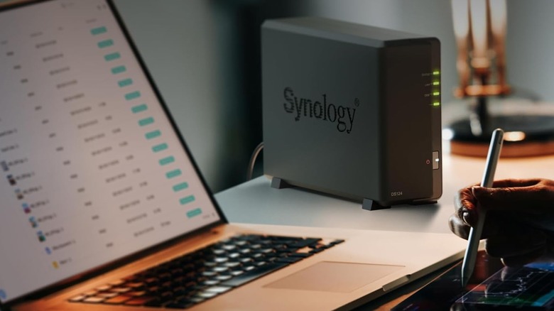 Synology NAS drive on a desk beside an open laptop
