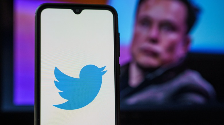 Twitter logo on phone near blurry Elon Musk
