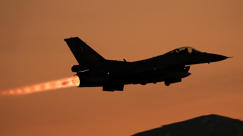 F-16 fighter taking off at sunset with afterburner glowing