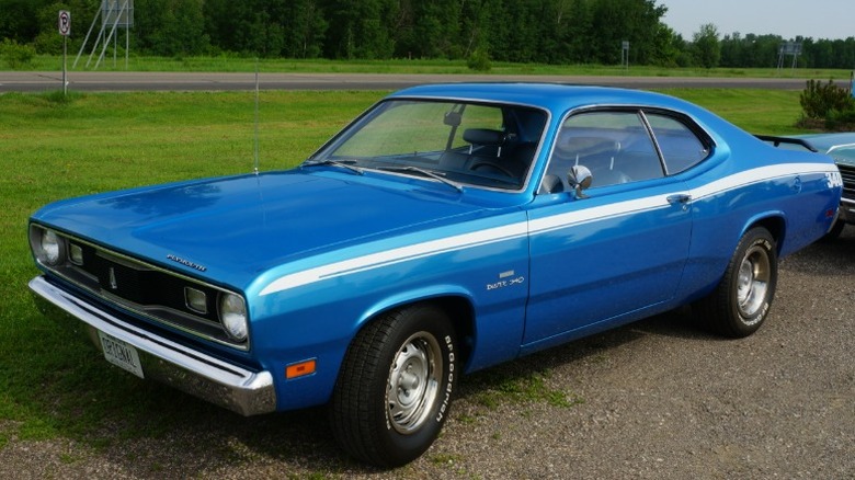 Blue Plymouth Duster 340 parked on gravel next to a rural road.