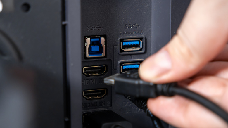 Close-up of a person's hand plugging a black HDMI cable