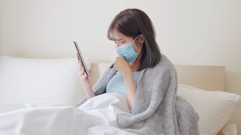 Person with mask on coughing and holding their smartphone