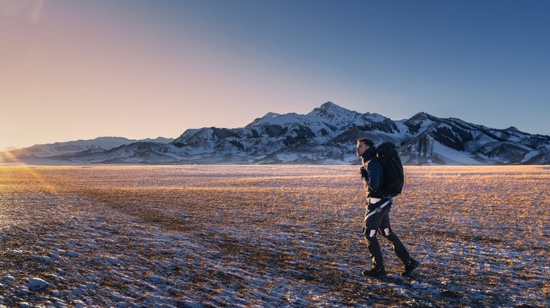 Man walking with Hypershell exoskeleton and wearing a ruck in snowy, mountainous terrain