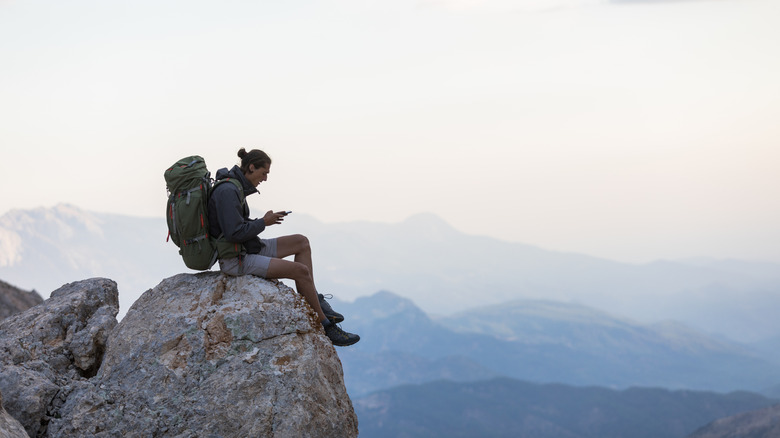 Man sitting on a cliff's edge and using his phone.