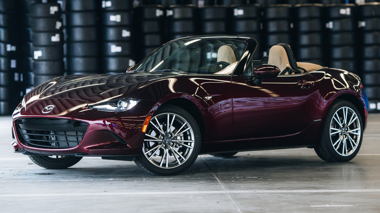 Front left view of purple 2025 Mazda Miata in garage with stacked tires in background