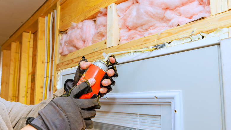 Person applies weatherproofing foam spray around door frame during home renovation