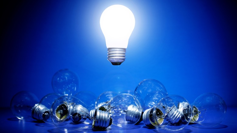 A brightly lit light bulb hovering over broken light bulbs