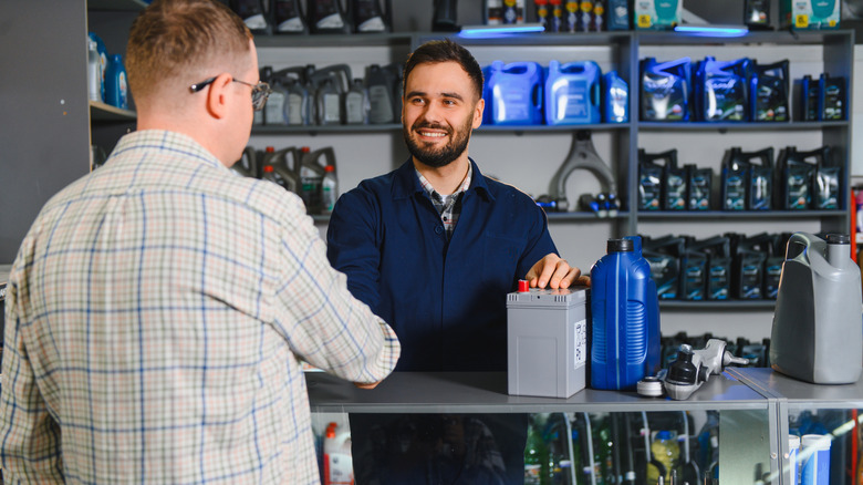 Seller recommending a car battery and engine oil to a customer in an auto parts store