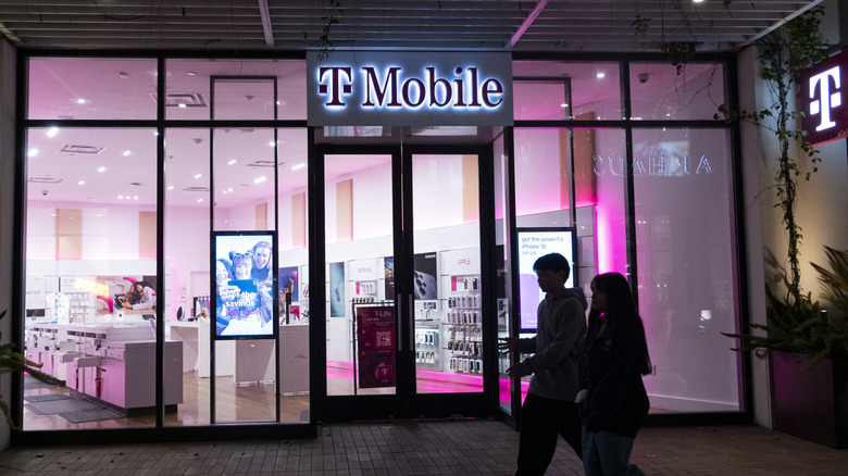 Shoppers in front of a T-Mobile sidewalk store with pink interior lighting