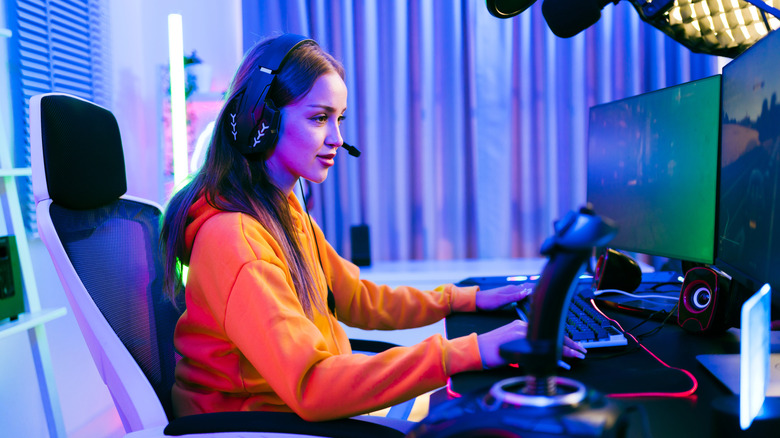 Gaming PC setup with young woman gamer, featuring multimonitor desktop, keyboard, mouse, and flight stick, right-side view