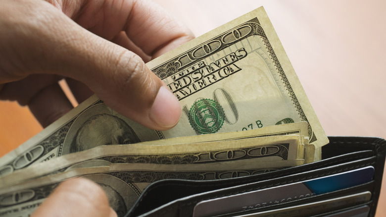 A Person Grabbing 100-US Dollar Bills Out Of A Wallet