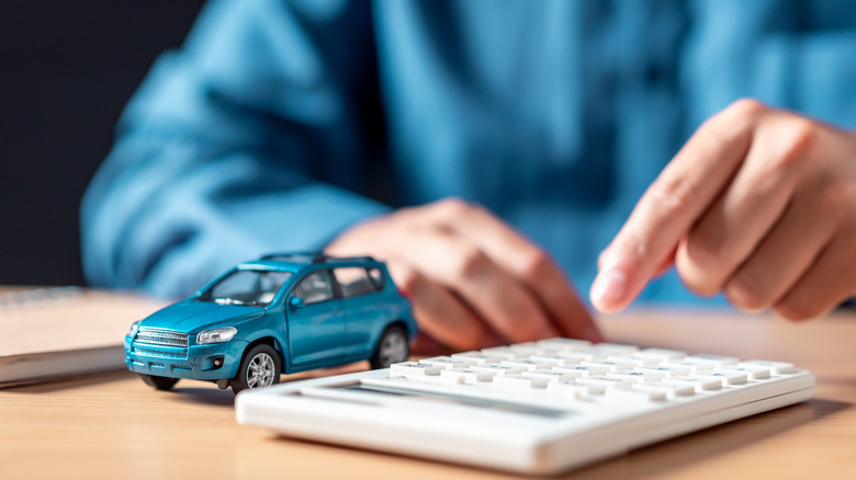 A man uses a calculator next to a toy car.