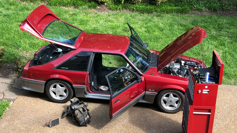 Fox Body Mustang with doors, hood, and trunk open, right side top down view, toolkit and parts in foreground