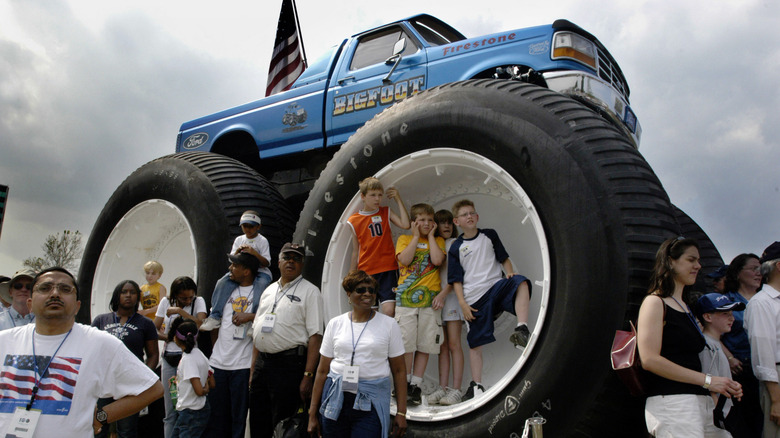 A bunch of people gathered around Bigfoot 5, with a few children inside the tires