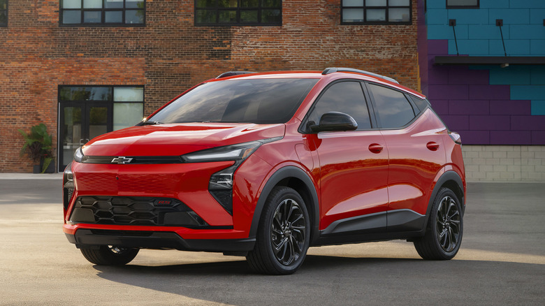 Front view of a red 2027 Chevrolet Bolt parked in front of a brick building