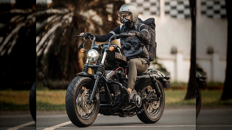 A biker wearing a backpack riding a Harley-Davidson.