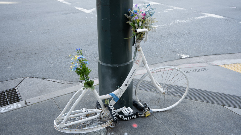 White memorial ghost bike bicycle with floral tributes secured to a lamppost at a busy intersection in the Mission Bay neighborhood, San Francisco, California