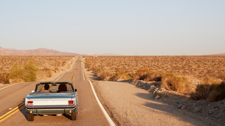Back shot of an old convertible driving down a desert highway.