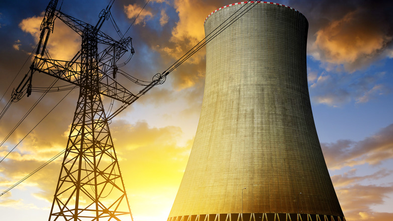 Nuclear power plant at sunset with high-voltage cables and pylons visible in the foreground