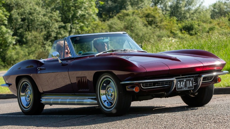 A maroon Chevrolet Corvette convertible with a man and woman in it.