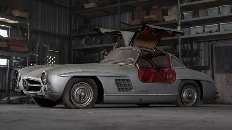 A silver 1956 Mercedes-Benz 300 SL with its gullwing doors open revealing the red leather interior
