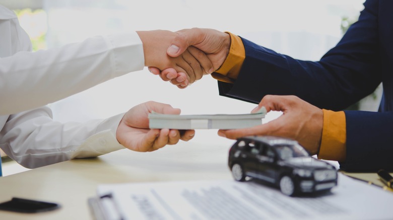 Two people shaking hands after signing the documents for a new car.