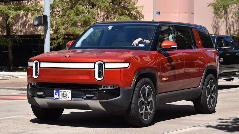 A red Rivian R1S SUV drives along the street