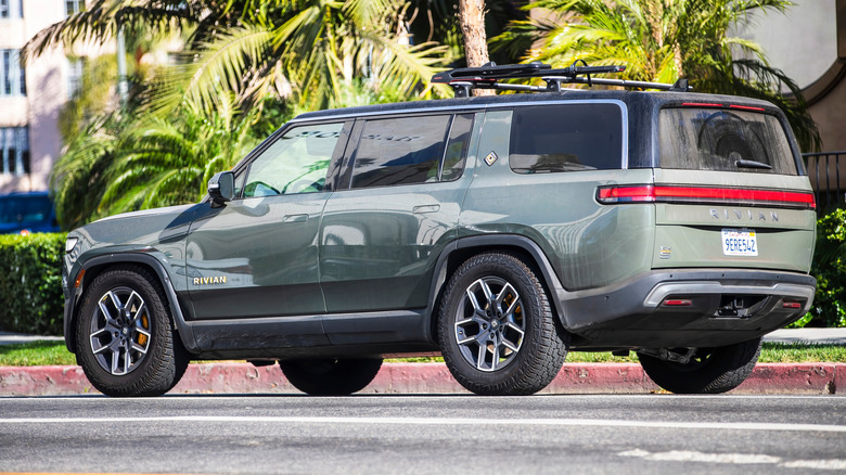 Green Rivian R1 parked on the side of the street with palm trees in the background
