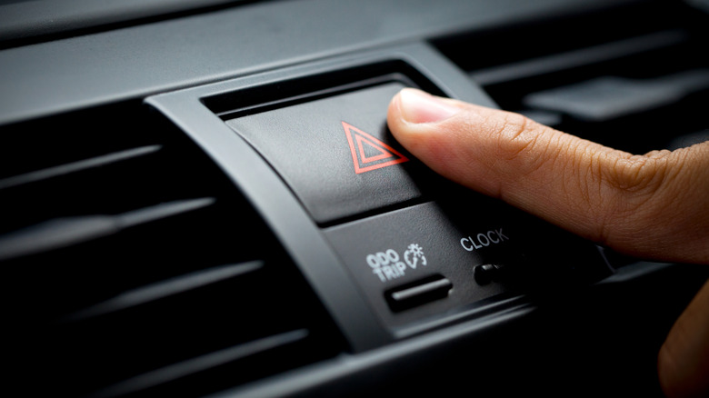 Finger on car's hazard lights button.