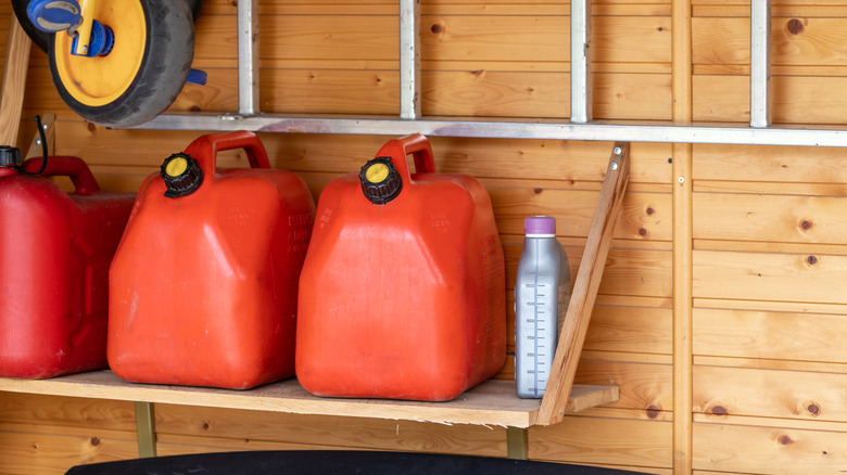 Three cans of gasoline placed upright on a wood shelf.