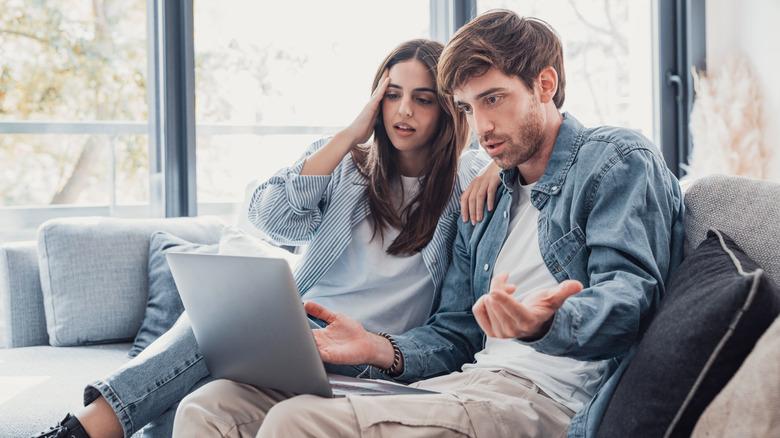 Two upset-looking people using a silver laptop.