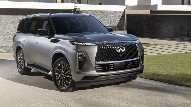 2025 Infiniti QX80 parked in driveway of modern home, front 3/4 view