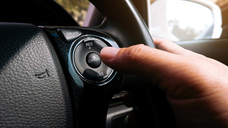 A close-up of a hand about to engage cruise control on a vehicle's steering wheel