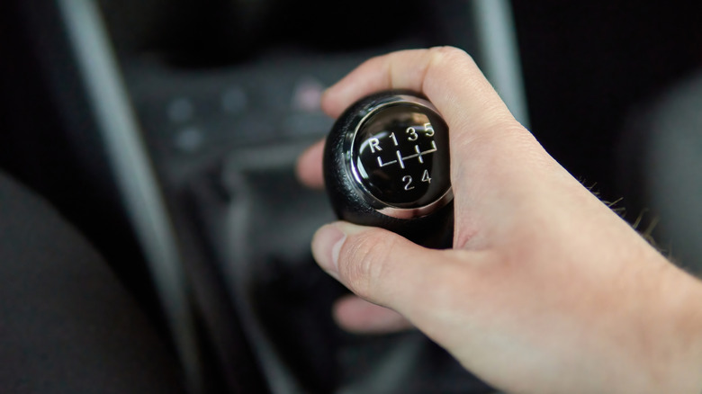A hand holding a manual transmission gear shifter inside the car.