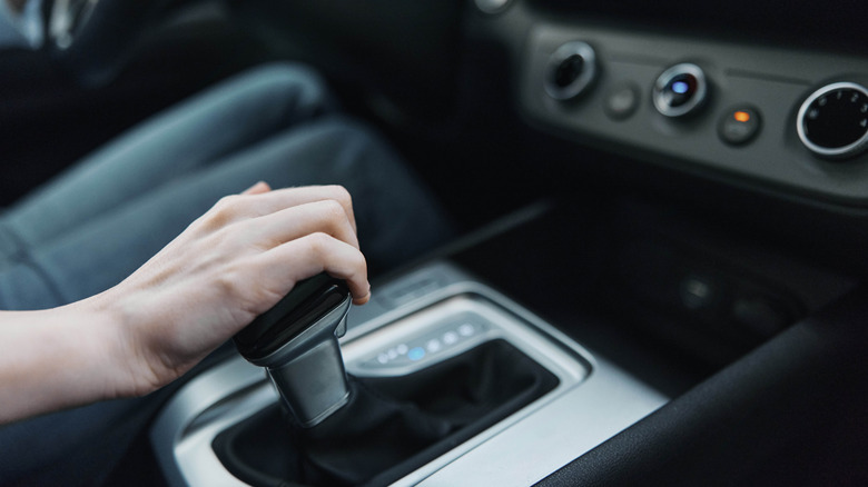 A driver's hand hovering over the gear shifter inside an automatic car.