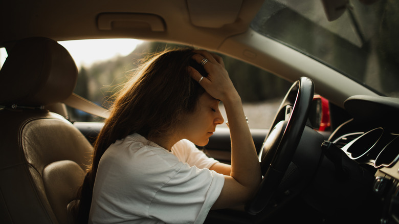 A woman sitting in the driver's seat of a car, resting her head on her hand