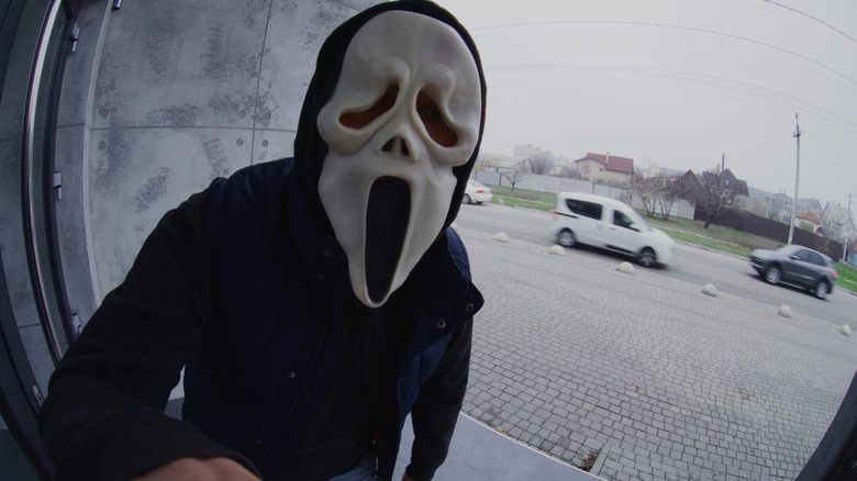 A doorbell camera captures a man wearing a ghost ask as he approaches someone's front door.