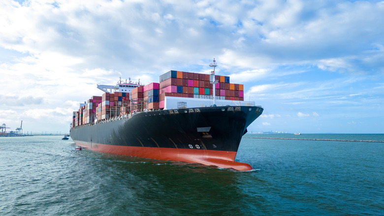 Aerial side view of cargo ship carrying containers and cutting through the water during the day