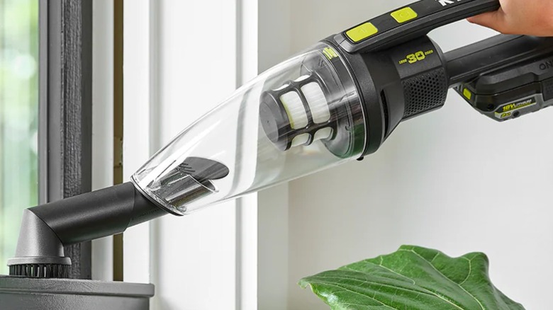 A person cleaning a window sill with a Ryobi hand vacuum