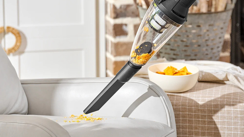 A person cleaning spilled chips off of a white couch with a Ryobi hand vacuum