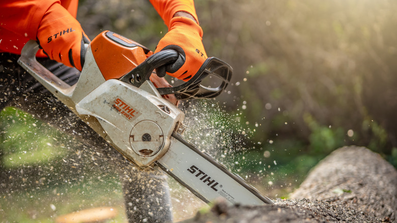 A close-up of woodcutter sawing wood with chainsaw as sawdust fly to sides.