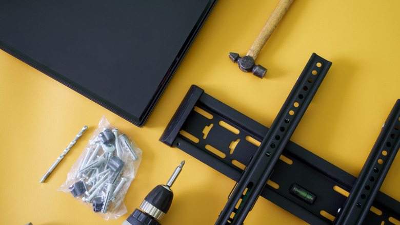 Tools and hardware for TV mounting on a surface.